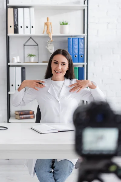Positive doctor talking near notebook and blurred digital camera in clinic — Stock Photo