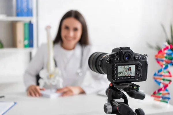 Médico desfocado segurando modelo espinhal perto de câmera digital no hospital — Fotografia de Stock