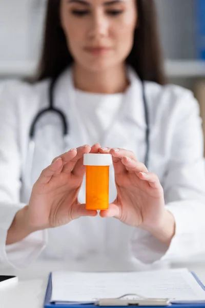 Blurred doctor holding pills near clipboard in clinic — Stockfoto