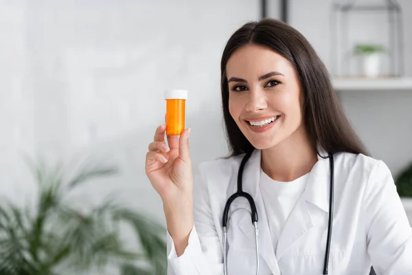 Веселий лікар тримає таблетки і дивиться на камеру в клініці — стокове фото