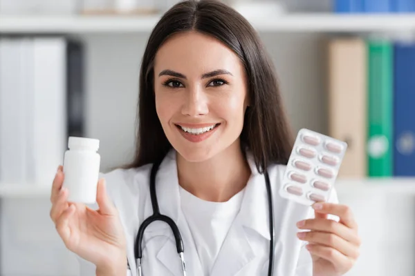 Fröhlicher Arzt hält Pillen in der Hand und blickt in Klinik in die Kamera — Stockfoto