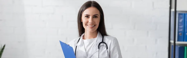 Smiling doctor holding clipboard in hospital, banner — Stock Photo
