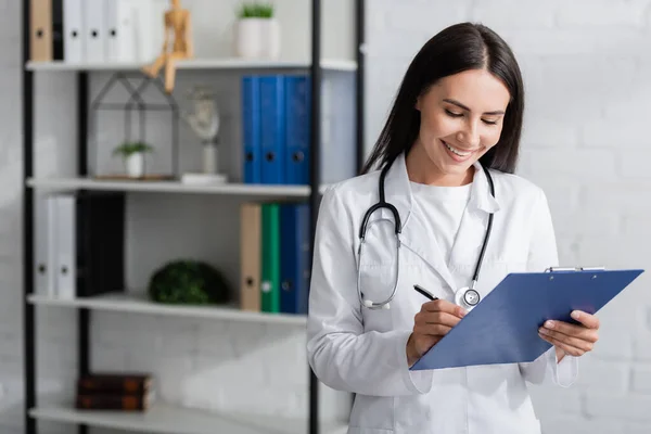Cheerful doctor writing on clipboard in hospital — Foto stock