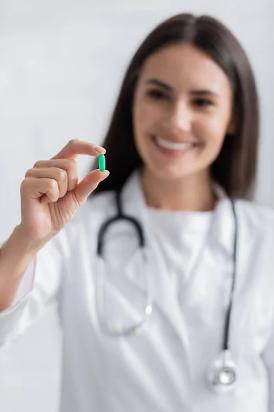 Brune floue médecin tenant pilule verte dans la clinique — Photo de stock