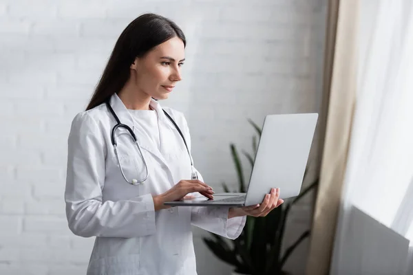 Brünette Ärztin mit Stethoskop mit Laptop in Klinik — Stockfoto