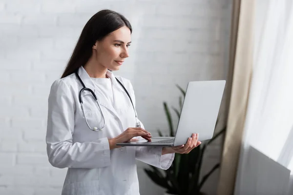 Medico bruno con stetoscopio utilizzando il computer portatile in clinica — Foto stock