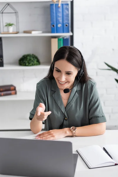 Insegnante sorridente in auricolare che punta al computer portatile durante la lezione online in classe — Foto stock