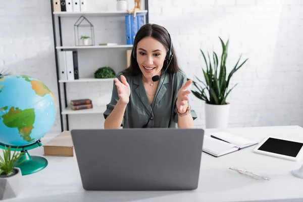 Teacher in headset having video call on laptop near book and globe in school — Foto stock