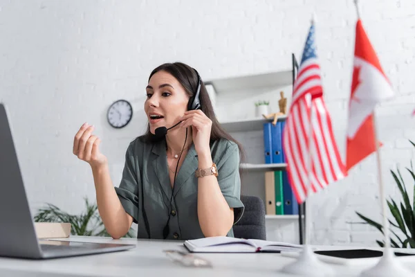 Teacher in headset having online lesson on laptop near blurred flags in school — Fotografia de Stock