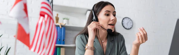 Teacher in headset talking near laptop and blurred flags in school, banner — Stock Photo