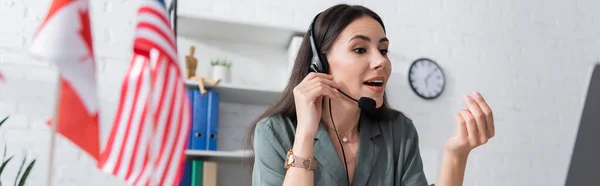 Teacher in headset talking near laptop and blurred flags in school, banner — Foto stock