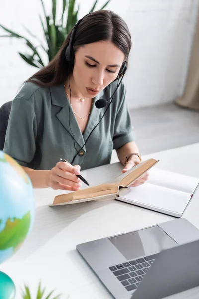 Teacher in headset reading book during online lesson on laptop in school — Stock Photo