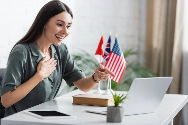 Positive teacher pointing with finger during online lesson on laptop in school — Stock Photo