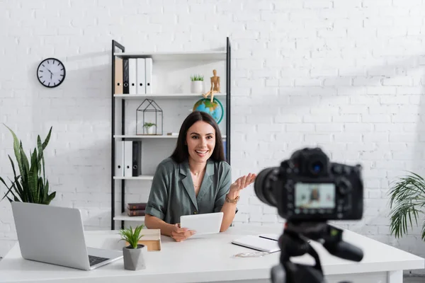 Smiling teacher holding digital tablet and talking near camera in classroom — Foto stock