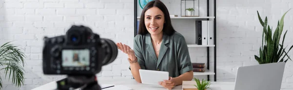 Positive teacher with digital tablet talking near blurred camera in school, banner — Foto stock