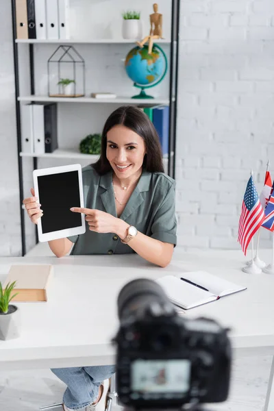 Insegnante indicando tablet digitale vicino fotocamera offuscata e bandiere in classe — Foto stock