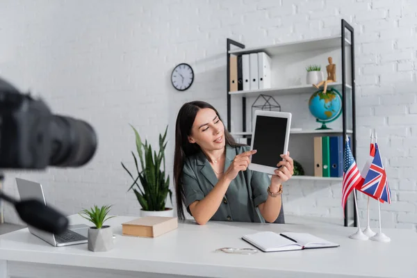 Tutor zeigt auf digitales Tablet neben Flaggen und verschwommener Kamera im Klassenzimmer — Stockfoto