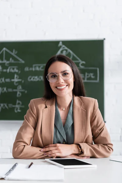 Insegnante positivo negli occhiali che guarda la fotocamera vicino al tablet digitale in classe — Foto stock