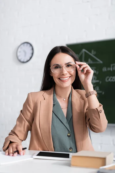 Positiver Lehrer mit Brille sitzt neben digitalem Tablet und Buch im Klassenzimmer — Stockfoto