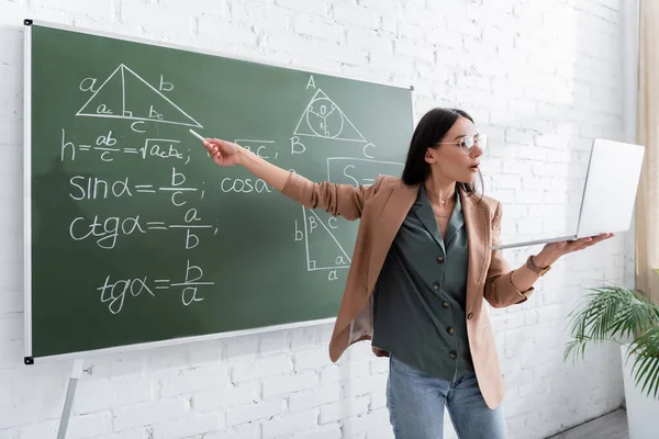 Enseignant pointant vers les formules mathématiques sur tableau pendant la leçon en ligne en classe — Photo de stock