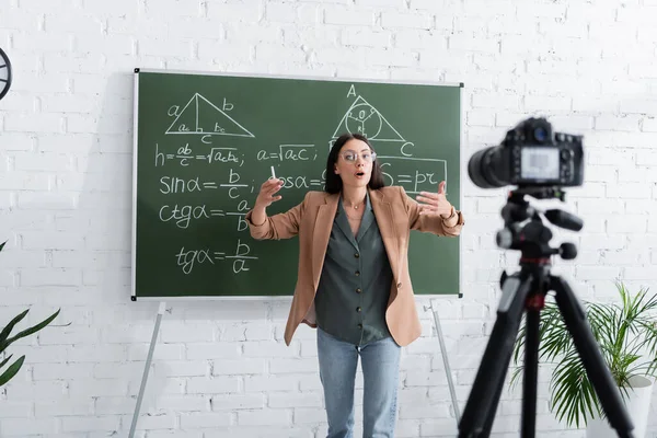 Enseignant parlant près de formules mathématiques sur tableau et appareil photo numérique en classe — Photo de stock