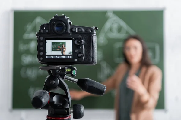 Blurred teacher standing near chalkboard and digital camera — Stock Photo