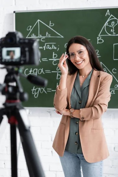 Professeur joyeux tenant craie près du tableau et appareil photo numérique dans la salle de classe — Photo de stock