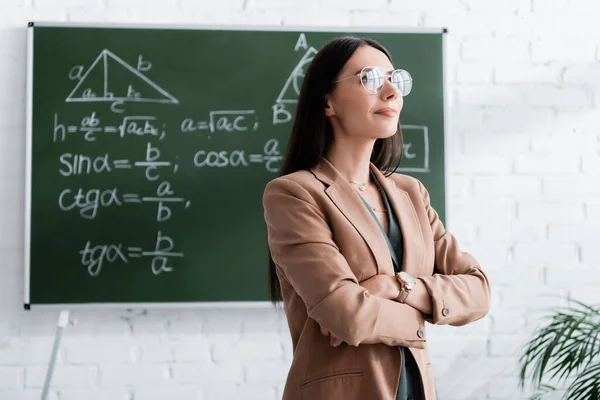 Вчителька в окулярах стоїть біля дошки в школі — стокове фото