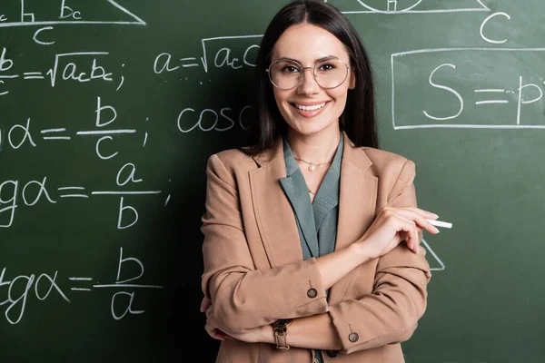 Positive teacher holding chalk near math formulas on chalkboard — Stock Photo