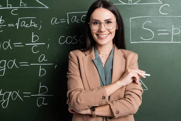 Professeur positif tenant la craie près des formules mathématiques sur tableau — Photo de stock