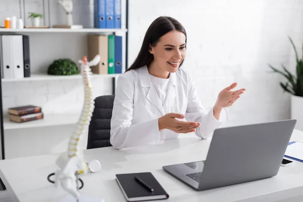 Smiling doctor pointing at laptop during online consultation in hospital - foto de stock