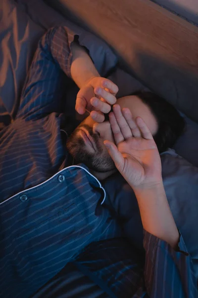 High angle view of man touching eyes while lying on bed — Foto stock