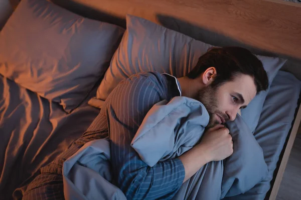 Vista superior del hombre en pijama que sufre de insomnio en la cama por la noche - foto de stock