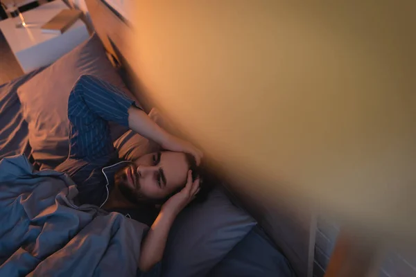 Top view of young man touching head while lying on bed at home — Foto stock