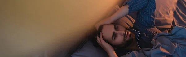 Draufsicht auf einen jungen Mann im Schlafanzug, der zu Hause mit dem Kopf auf dem Bett liegt, Banner — Stockfoto
