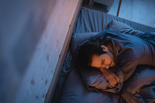 Top view of young man lying on pillow and looking away at night — Stockfoto