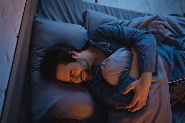 Top view of depressed man holding pillow while lying on bed — Stockfoto