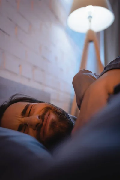 Upset man closing eyes while lying on bed at night — Stock Photo