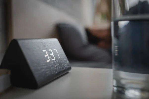 Close up view of electronic alarm clock near glass of water in bedroom — Stock Photo