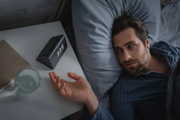 Vue de dessus de l'homme avec insomnie regardant réveil électronique sur la table de chevet — Photo de stock