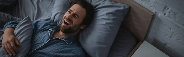 Vue du dessus de l'homme en pyjama bâillant sur le lit le matin, bannière — Photo de stock