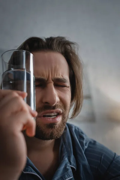 Erschöpfter Mann hält Glas Wasser in der Hand, während er zu Hause an Schlaflosigkeit leidet — Stockfoto
