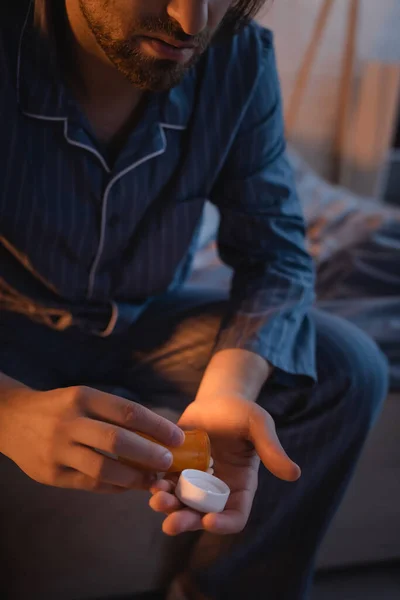 Vista recortada del hombre con trastorno del sueño sosteniendo pastillas en la cama por la noche - foto de stock