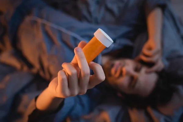 Top view of blurred man with sleep disorder holding jar with pills in bedroom - foto de stock