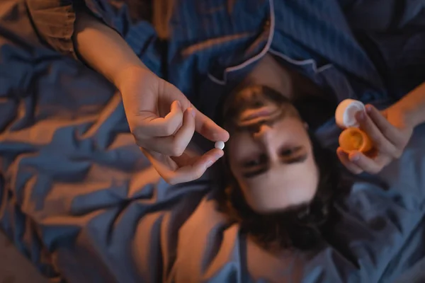 Top view of blurred man holding pill on bed at night - foto de stock