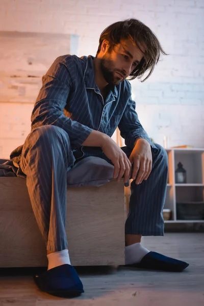 Расстроенный мужчина в пижаме сидит на кровати ночью — стоковое фото
