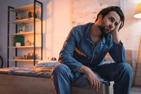 Cansado homem em pijama sentado na cama à noite — Fotografia de Stock