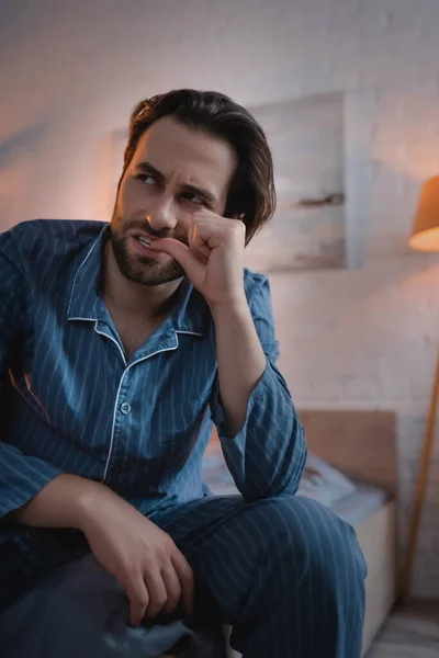 Stressed man in pajamas biting nail on hand on bed at night — Stock Photo