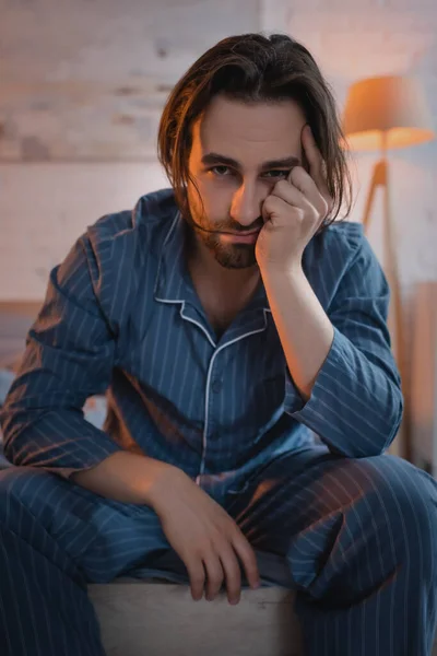 Upset man in pajamas looking at camera while sitting on bed at night — Photo de stock