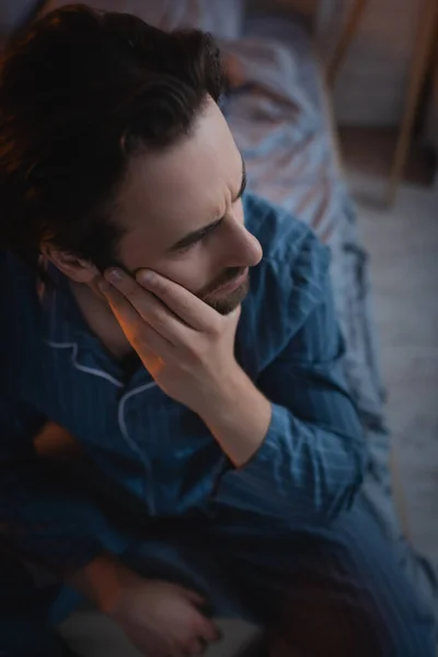 High angle view of stressed man with insomnia looking away while sitting on bed at night - foto de stock